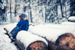 Kids having fun in forest on winter day. Resting on snow covered tree trunks.